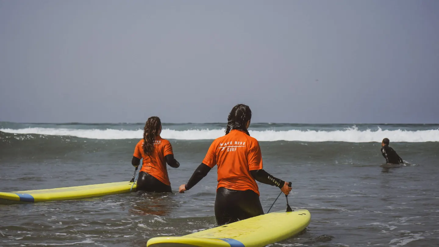An instructor walking a young surfer out into the whitewater in Agadir
