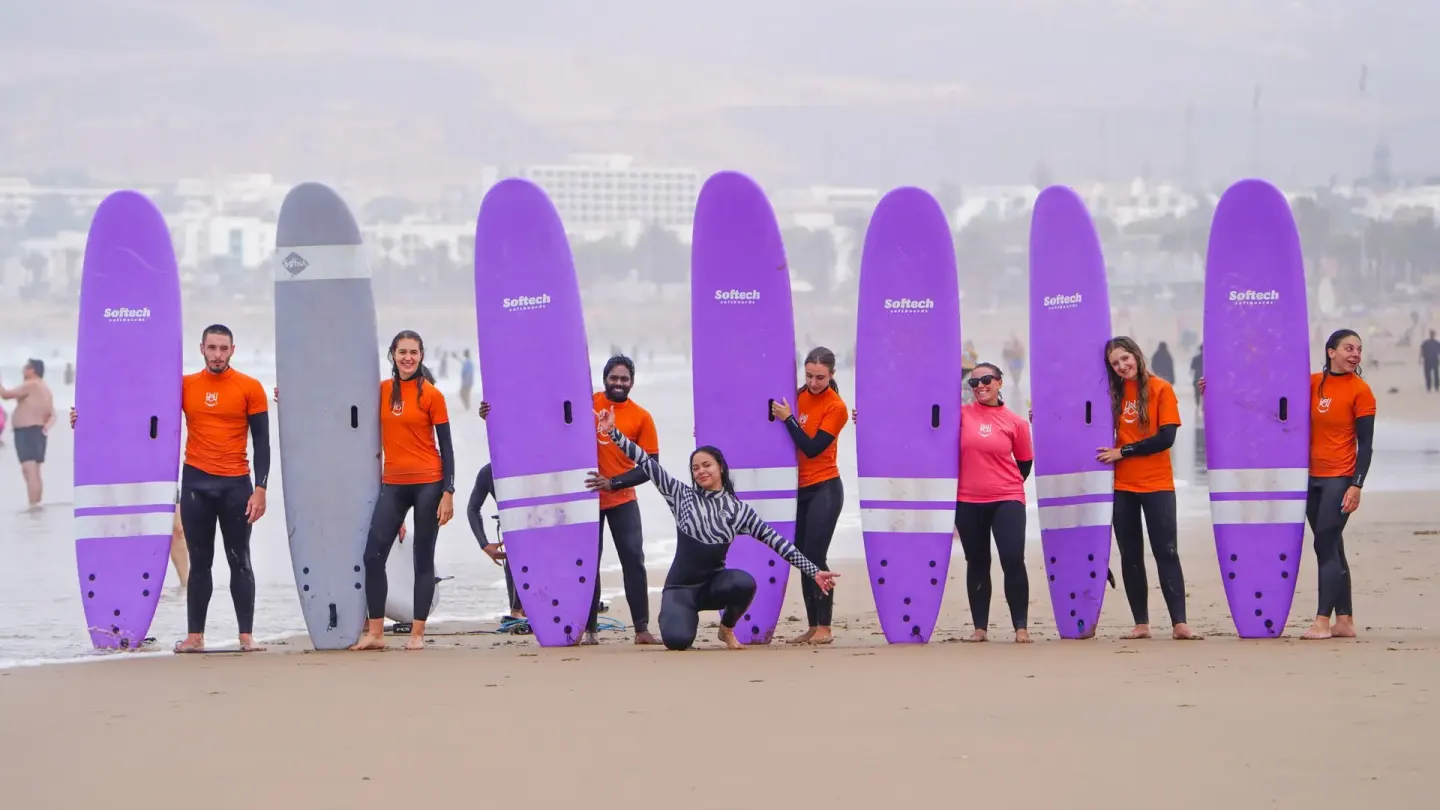 Surfers standing behind a row of soft-top boards planted in the sand