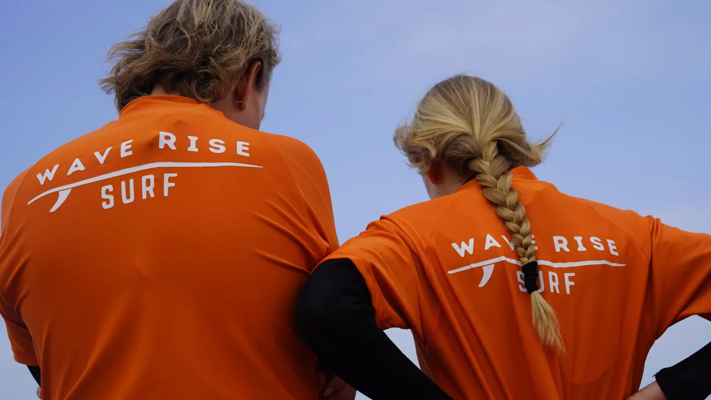 Two Wave Rise instructors in branded tops looking out at the ocean